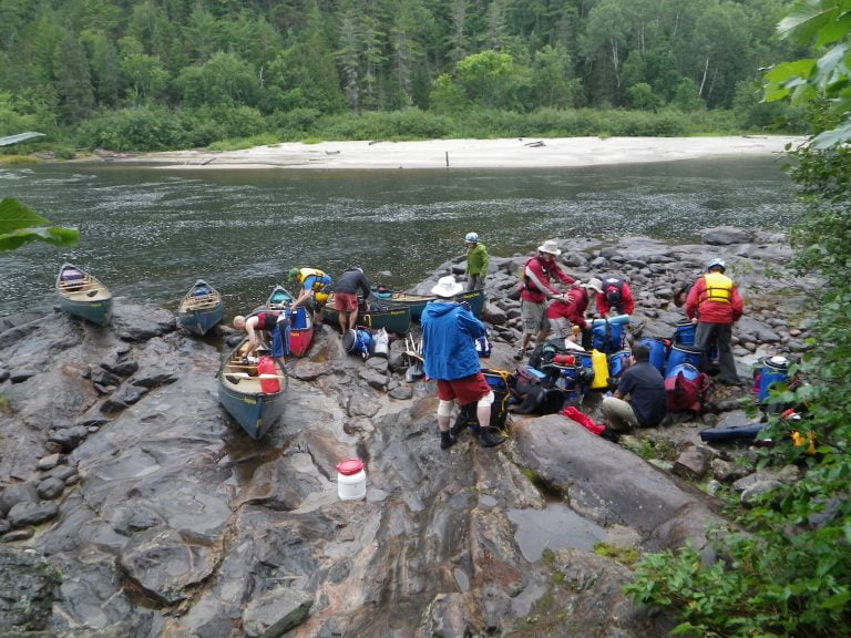 Paddlers loading canoes with gear on rocky shore