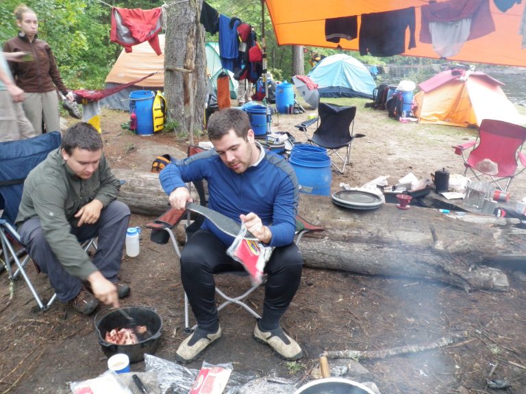 Campers cutting bacon package with machete and cooking bacon