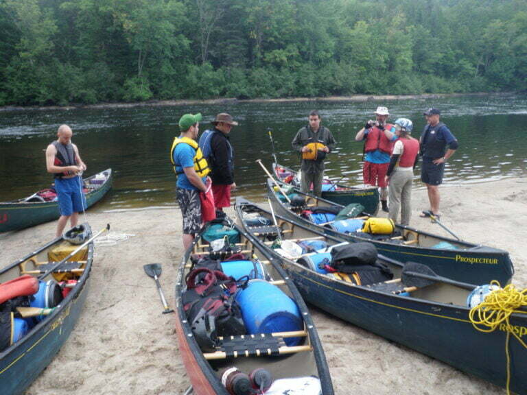 Group of paddlers ready to depart, canoes loaded on shore