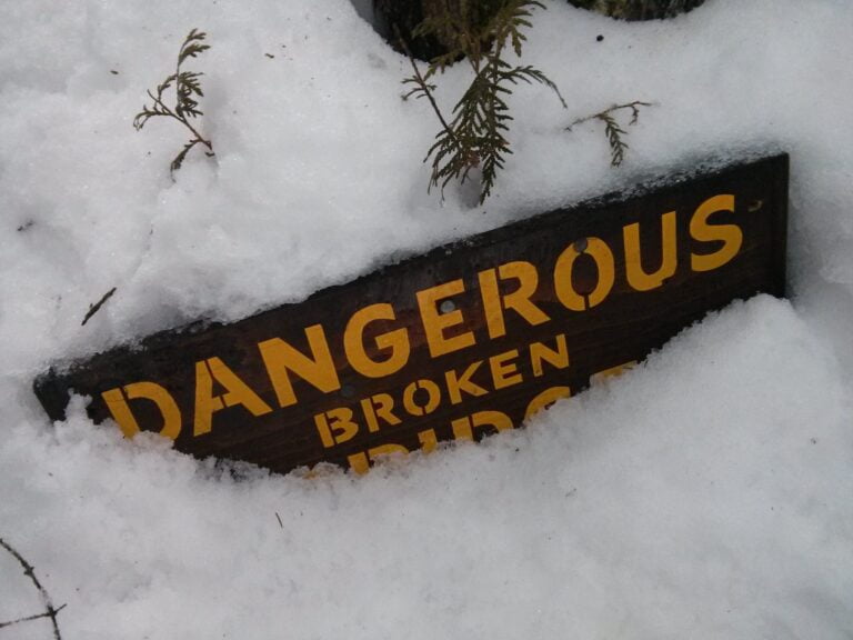 Sign indicating a danger due to broken bridge half buried in snow