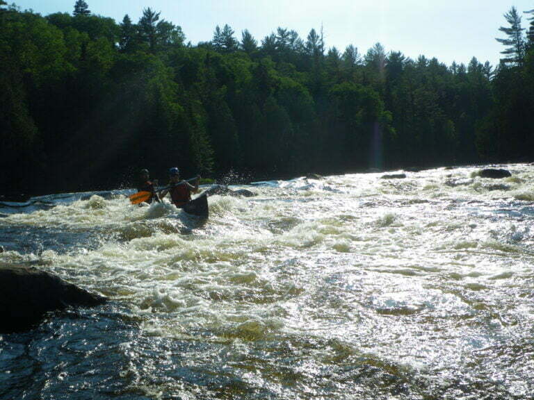 Tandem canoe in whitewater rapids with water splashing over canoe