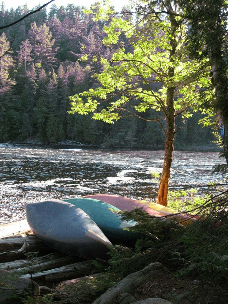 three canoes turned on their sides on shore next to a river during sunset