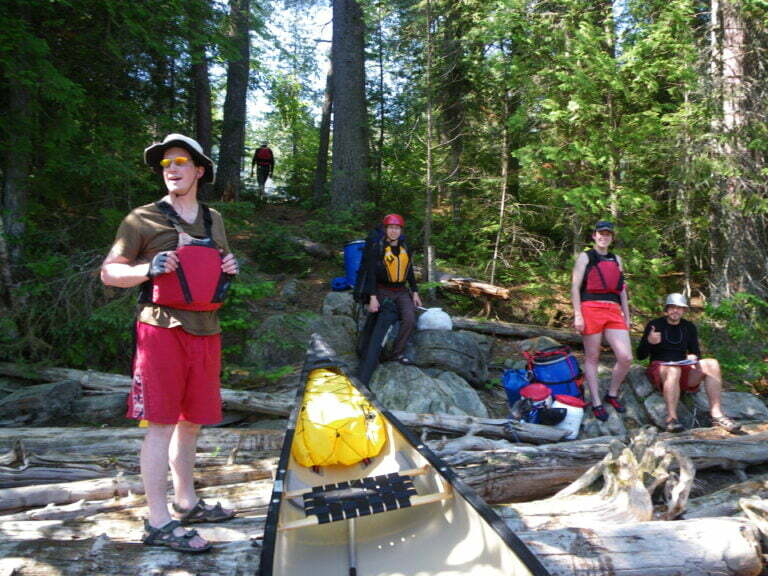 Group in the forest, sitting on rocks and bringing equipment to canoes