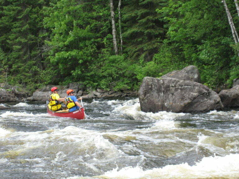 tandem canoe in whitewater heading down a rapid backwards with both paddlers looking back towards bottom of rapid