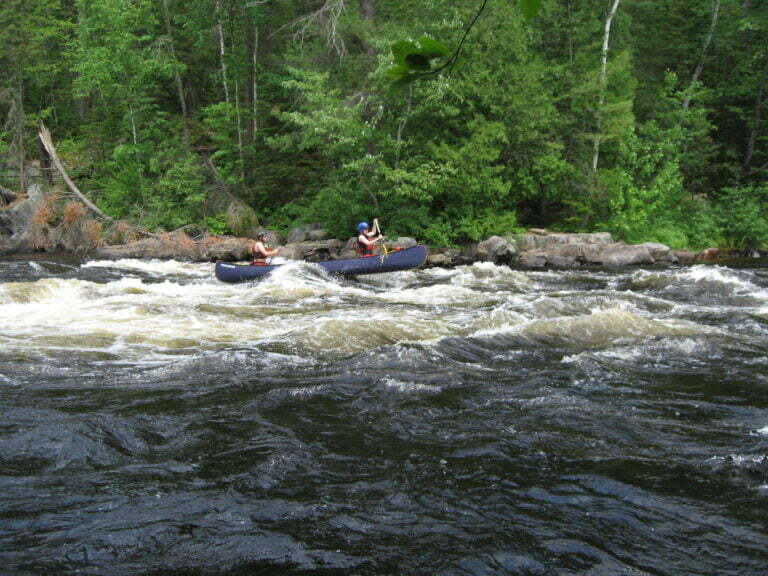 Canoe riding a wave with front of canoe mid-air in rapid