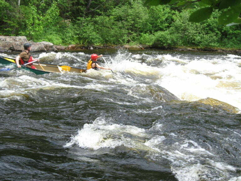 canoe just on the edge of large wave and drop in rapids