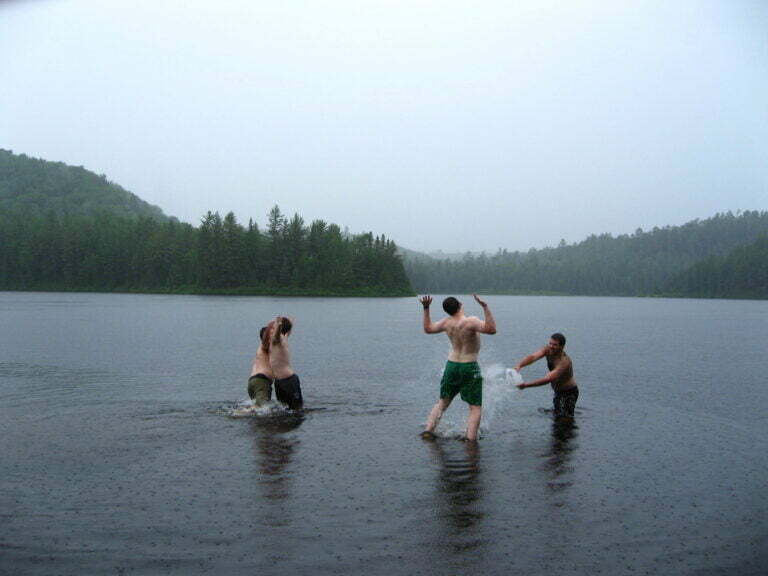 Group of men in bathing suits waist deep in river, jumping, hugging and throwing water 
