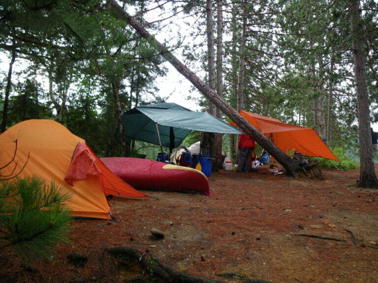 campsite with canoe on the ground, tents and guide tarps as rain shelters