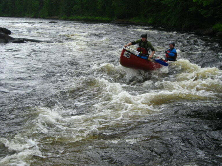 canoe riding waves in rapid with bow in the air
